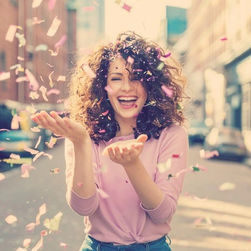 A woman with curly hair celebrating with confetti